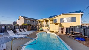 A pool area with lounge chairs and a picnic table, surrounded by wooden fences and a building with a sloped roof.