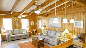 A cozy cabin interior with wooden walls, two sofas, a dining table, and a ceiling fan.