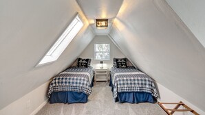A small attic bedroom with two beds, a desk, and a window. - Lovely Lake View 4 BR Cabin w/ Large Kitchen & Deck. Across from lake access (Lake Arrowhead)