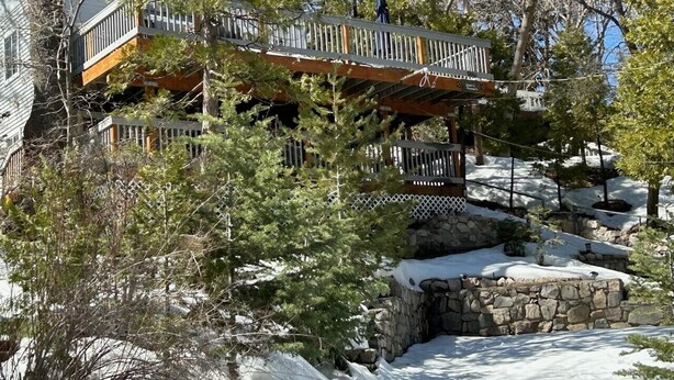 A multi-level cabin with a stone foundation, wooden deck, and a view of a snowy landscape. - Lovely Lake View 4 BR Cabin w/ Large Kitchen & Deck. Across from lake access (Lake Arrowhead)