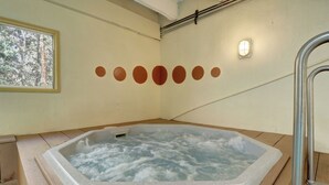 A hot tub with a wooden floor surrounding it, a window with a forest view, and a wall with circular decorations. - 2 Bedroom Condo Just off Frisco Main Street. B207 (Frisco)