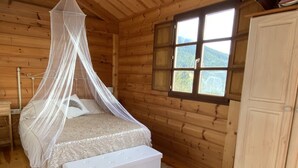 Ein Schlafzimmer in einer Holzhütte mit einem Bett unter einem Moskitonetz, einem Fenster mit Blick und einem Schrank.