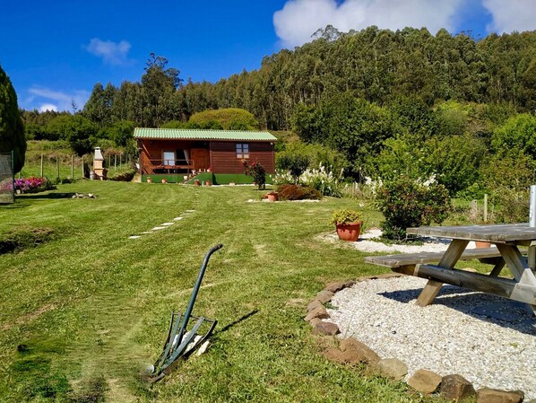 Une cabane en bois avec un toit vert, entourée d’une pelouse bien entretenue et d’une table de pique-nique.