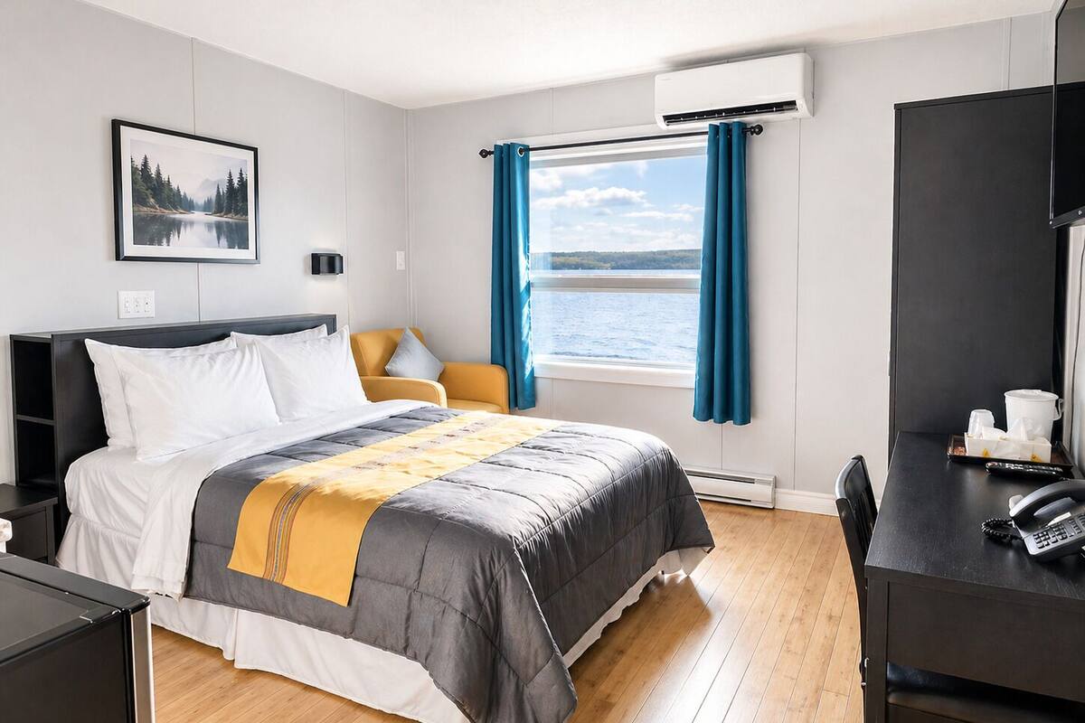 Habitación de hotel con cama, escritorio, silla, ventana con cortinas, un cuadro en la pared y un equipo de aire acondicionado.