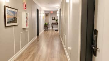 A hotel hallway with wooden flooring, white walls, and a framed picture.