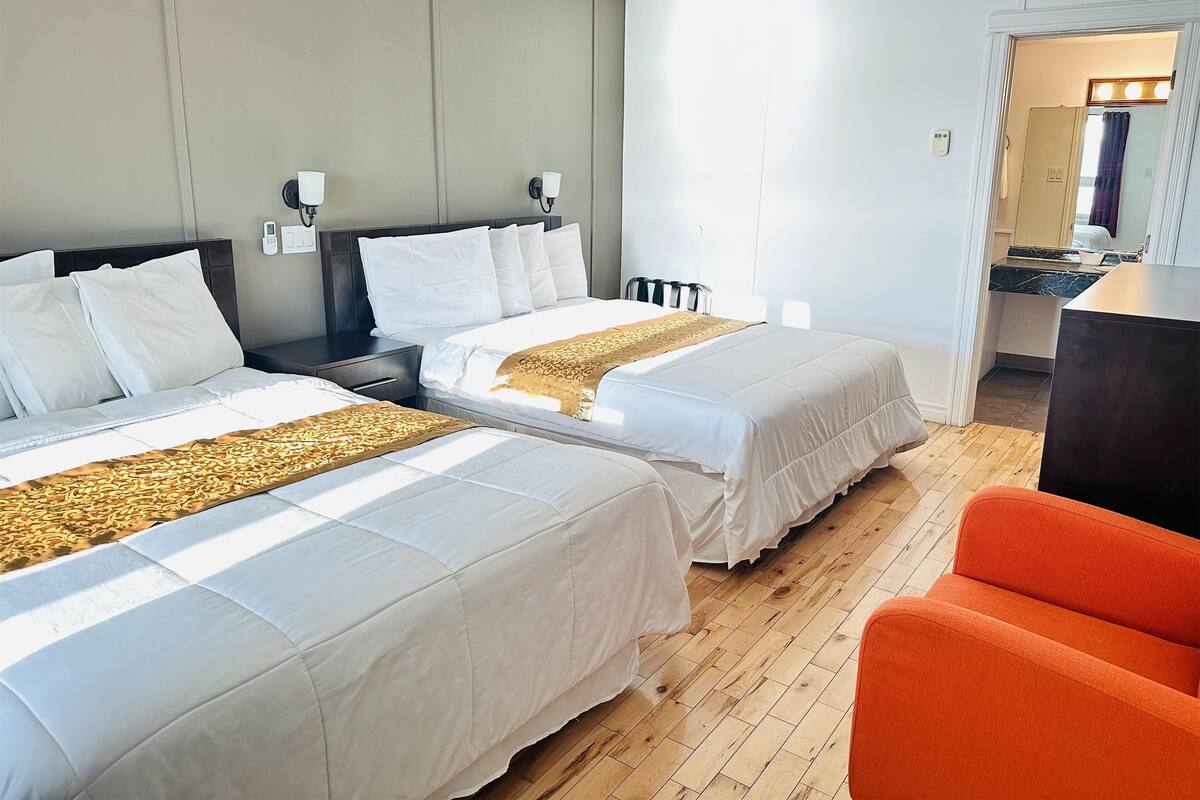 Habitación de hotel con dos camas, suelo de madera, un escritorio y un baño visible a través de una puerta abierta.