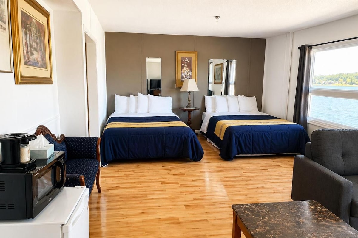 Habitación de hotel con dos camas, un escritorio, una silla, una mesa y vista al mar.