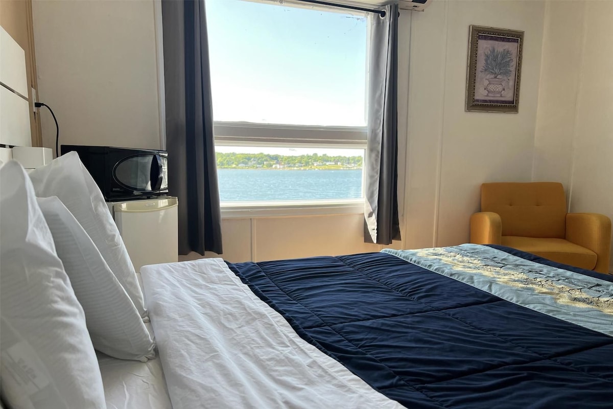 Habitación de hotel con cama, una silla, televisión y ventana con vista a un cuerpo de agua.