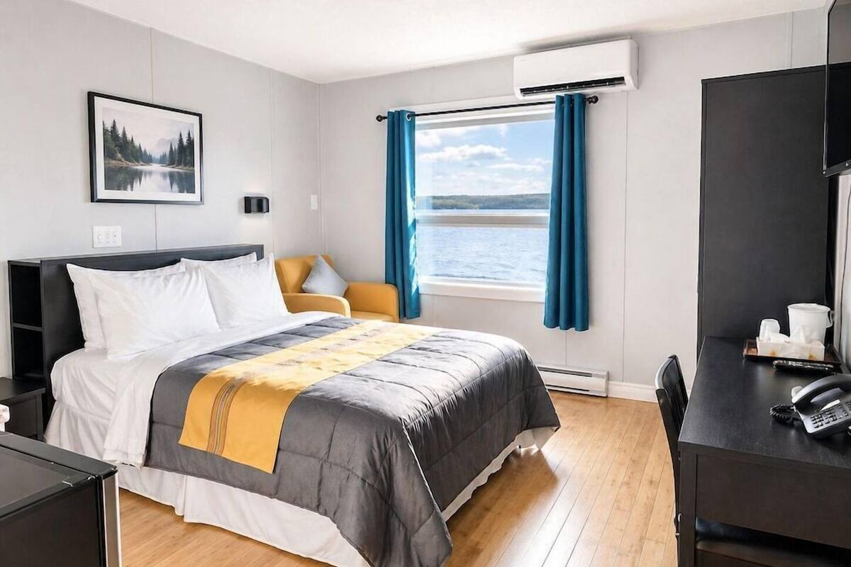 Habitación de hotel con cama, escritorio, silla, ventana con cortinas, aire acondicionado y un cuadro en la pared.