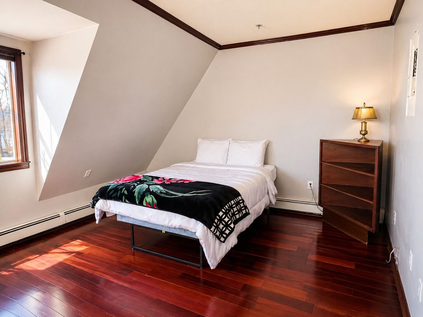 A bedroom with a bed, a nightstand, a lamp, and a wooden floor.