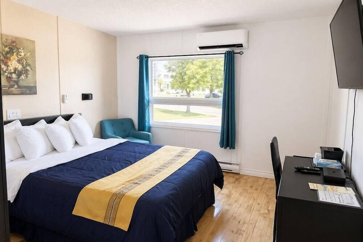 Habitación de hotel con cama, escritorio, silla, ventana con cortinas y unidad de aire acondicionado.
