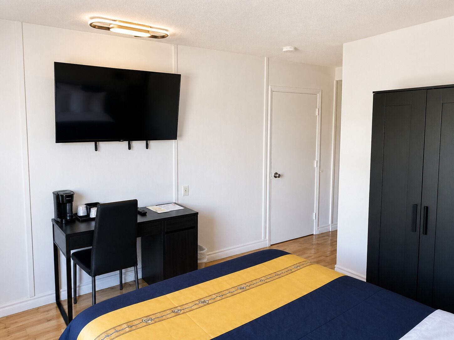 Une chambre d’hôtel comprenant un lit, un bureau avec une chaise, un téléviseur à écran plat et une armoire.
