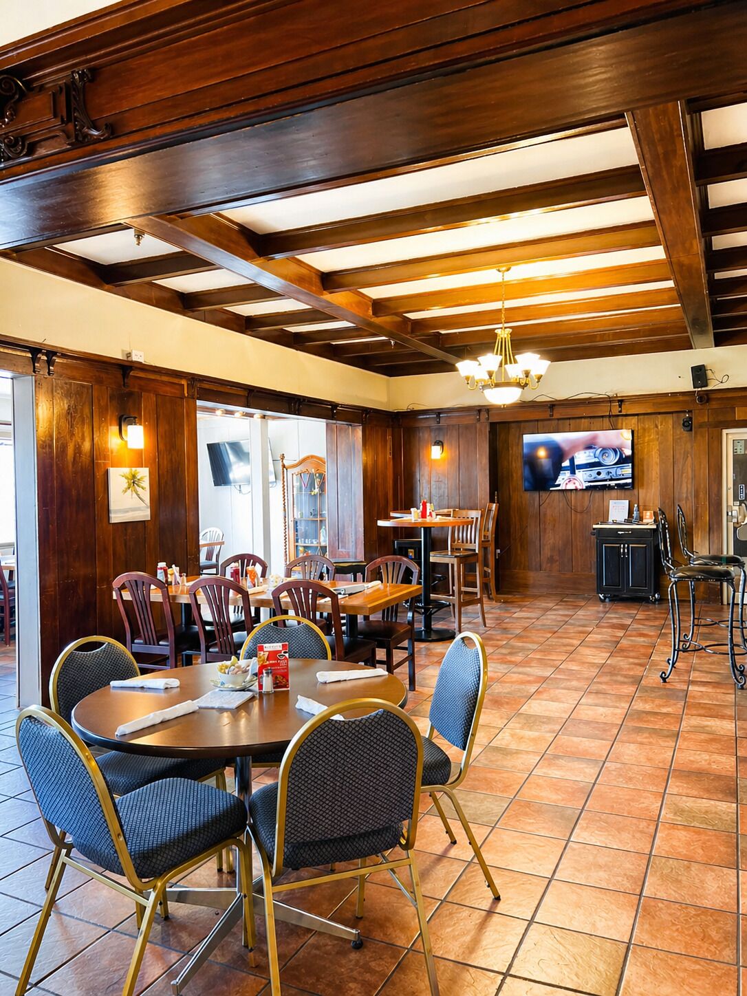 A restaurant with wooden beams, tiled flooring, and a TV mounted on the wall.