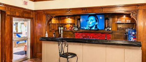 A bar area with a television, bar stools, and a red counter.