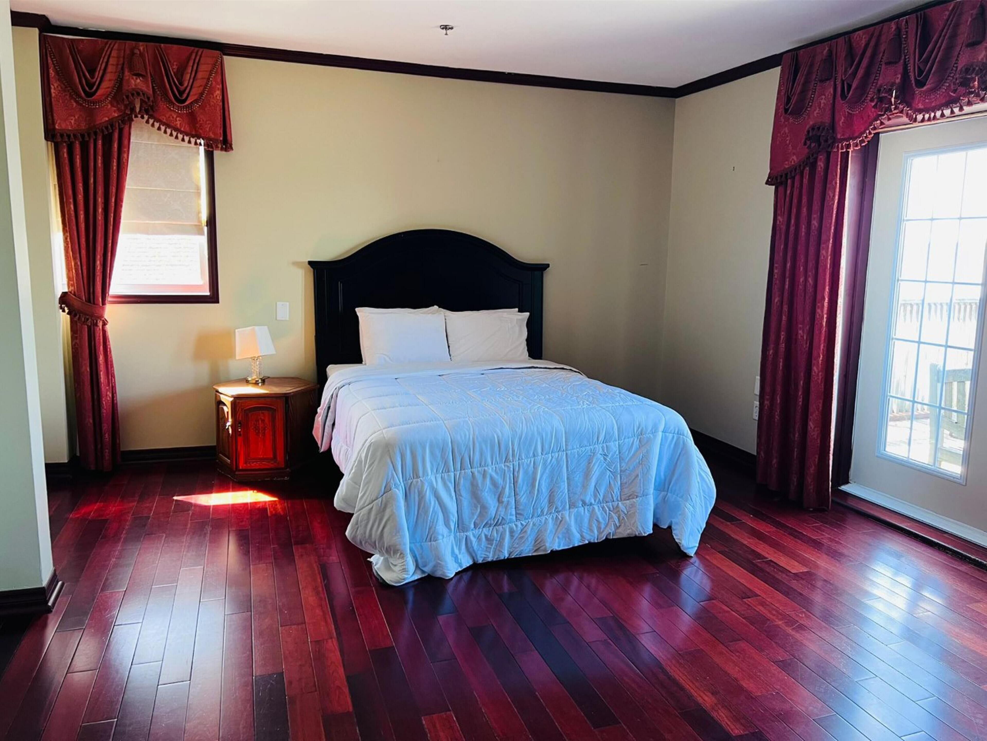 Um quarto com cama, mesa de cabeceira, janela com cortinas e porta.