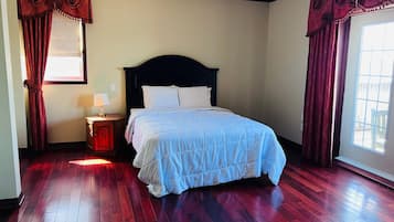 Um quarto com cama, mesa de cabeceira, janela com cortinas e porta.