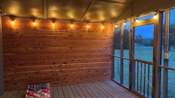 A wooden deck with a view of a grassy area, a string of lights, and a flag on the floor.