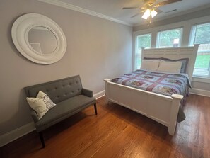 Une chambre à coucher avec un lit, un canapé gris, un miroir rond et un ventilateur de plafond.