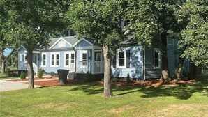 A row of blue houses with white trim, surrounded by trees and a well-maintained lawn.