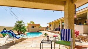 Zona de piscina con sillones reclinables, una pequeña mesa con una botella y una vista de una casa al fondo.