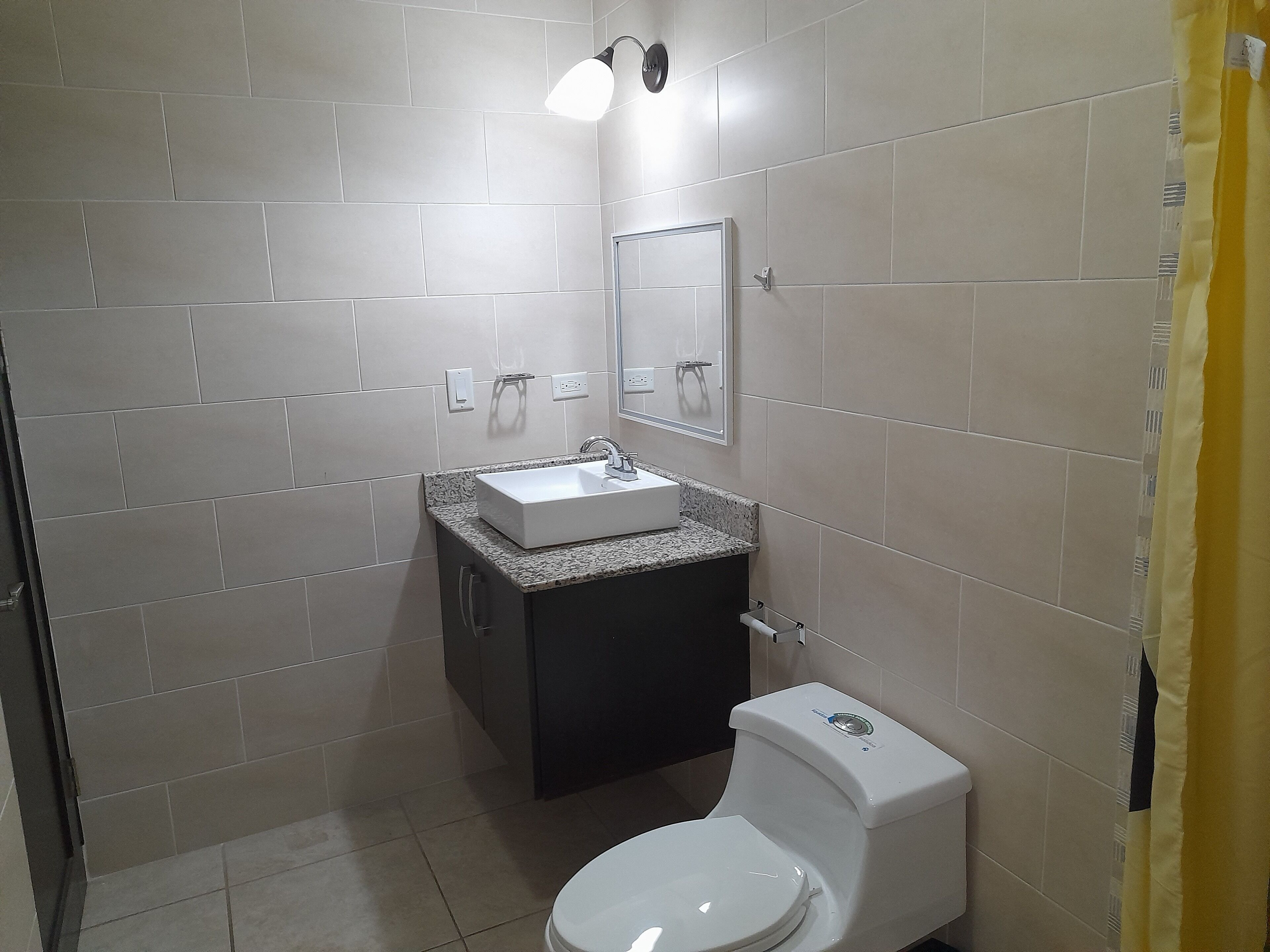 Un baño pequeño con lavamanos blanco, mueble oscuro y retrete.