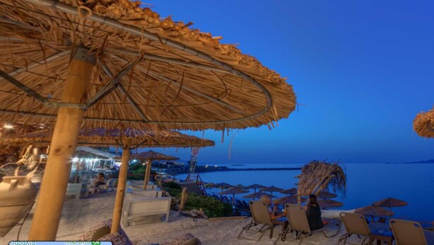 Een strandlounge met rieten parasols en ligstoelen met uitzicht op de zee.