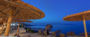 Een strandlounge met rieten parasols en ligstoelen met uitzicht op de zee.