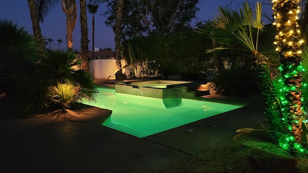 A swimming pool with a hot tub, surrounded by palm trees and greenery, at night. - Loving life! (Indian Wells)