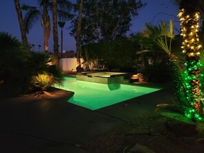 A swimming pool with a hot tub, surrounded by palm trees and greenery, at night. - Loving life! (Indian Wells)