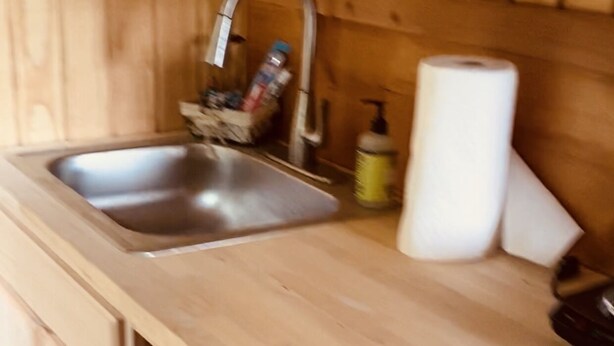 A kitchen with a wooden countertop, a stainless steel sink, a roll of paper towels, and a trash bin. - The Cabin at Crosswind Ranch  (Comanche)