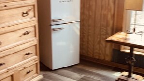 A compact kitchen with a white refrigerator, wooden cabinets, and a small dining table. - The Cabin at Crosswind Ranch  (Comanche)