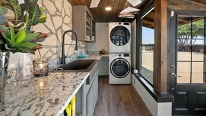 Een kleine wasruimte met een wasmachine, een wasbak en een raam met uitzicht op de omgeving.
