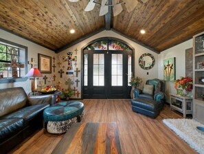 Relax in this inviting living room with a black leather sofa, blue armchair, and round ottoman, surrounded by beautiful artwork and a stunning stained glass window.