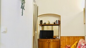 Una camera accogliente con un letto, una televisione su un mobile in legno e un piccolo ripiano con libri e oggetti decorativi.