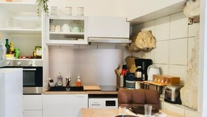Una cucina compatta con mobili bianchi, forno integrato, microonde e macchina da caffè. C'è un tavolo da pranzo con una sedia marrone e una grande decorazione a forma di roccia sulla parete.
