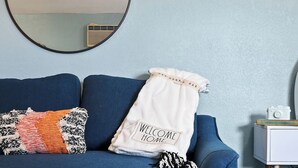 A room with a blue sofa, a round mirror, and a white pillow with "WELCOME HOME" text. - Adorable guest suite with private pool and entrance. (Lake Alfred)