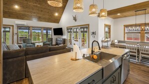 Een ruime woonkamer met een groot houten plafond, een geïntegreerde keuken met een spoelbak en een zithoek met een bank en stoelen.