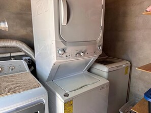 A laundry room with a stacked washer and dryer, a control panel, and a hose.