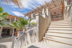 Un escalier menant à un bâtiment doté d’un espace extérieur abrité, de palmiers et surplombant un ciel dégagé.