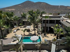 A resort with a pool, palm trees, and a mountainous backdrop.