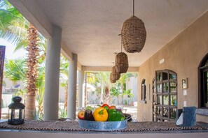 Un espace extérieur abrité, avec un saladier en métal rempli de fruits, une lanterne et un luminaire suspendu en osier.