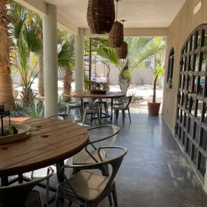 Un espace extérieur aménagé en terrasse, avec des tables et des chaises, entouré de palmiers et doté d’un sol en béton.
