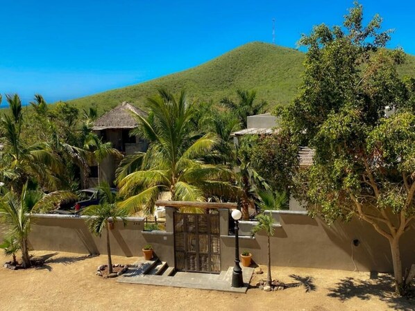 Un resort con vista a la playa, palmeras y una colina al fondo.