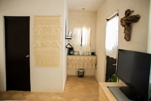 Un couloir avec une porte noire, un téléviseur fixé au mur, une décoration murale, une petite table avec une machine à café et une fenêtre avec des rideaux.