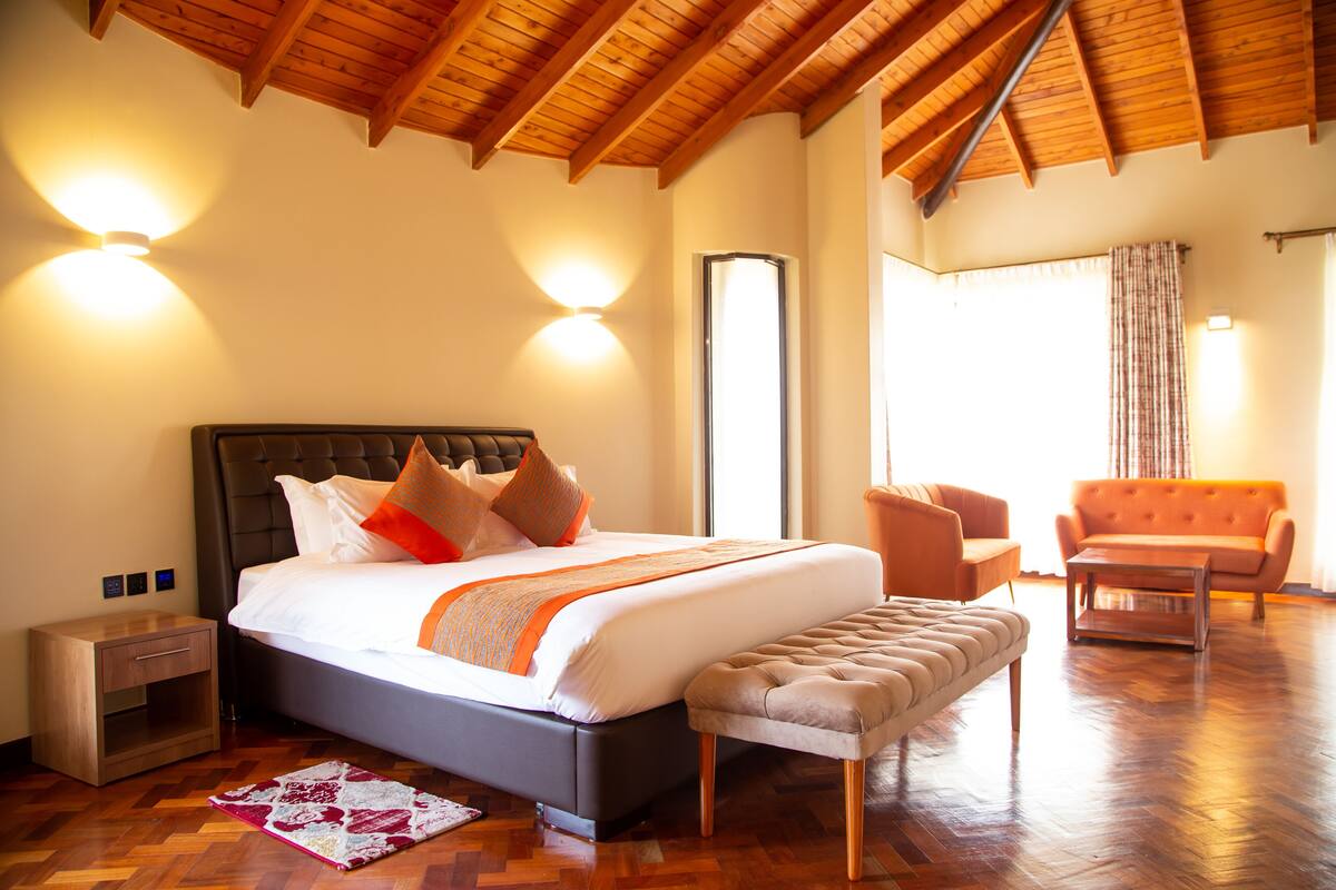 Un dormitorio espacioso con una cama grande, una mesita de noche, un banco, un sofá y techo de madera.