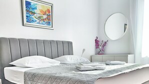 A modern bedroom with a grey upholstered bed, a quilted grey blanket, a bedside table with a vase of flowers, and a painting on the wall. - Top location (150 m- Bacvice, 400 m-Diocletian’s Palace, 5-minute walk to ferry) (Split)