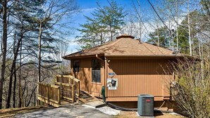Une petite cabane en bois avec un porche, une poubelle et un panneau indiquant un risque de présence d’ours.