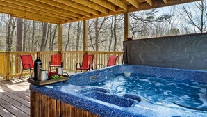 Une terrasse en bois avec un jacuzzi, des chaises rouges et une table où sont disposées des boissons et des fruits.