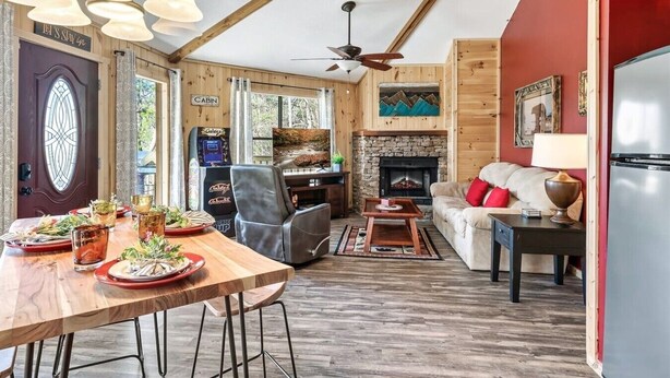 L’intérieur d’une cabane comprenant une table à manger, des chaises, un canapé, une cheminée et un ventilateur de plafond.