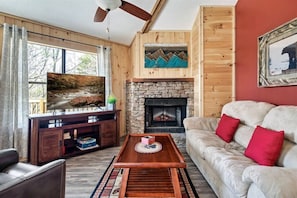 A cozy living room with a stone fireplace, wooden walls, a television, and a sofa with red cushions.
